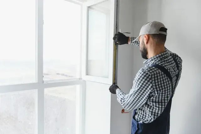Técnico taladrando el marco de una ventana junto a una ventana interior de color blanco brillante.