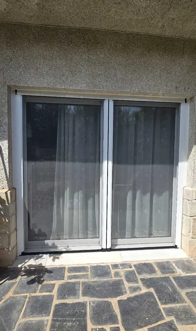 Puertas corredizas de cristal con cortinas blancas, enmarcadas por muros de piedra y un patio embaldosado.