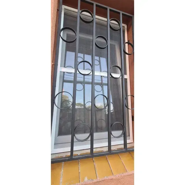 Rejas de seguridad de metal negro sobre una ventana blanca con alféizar amarillo y pared de ladrillo.