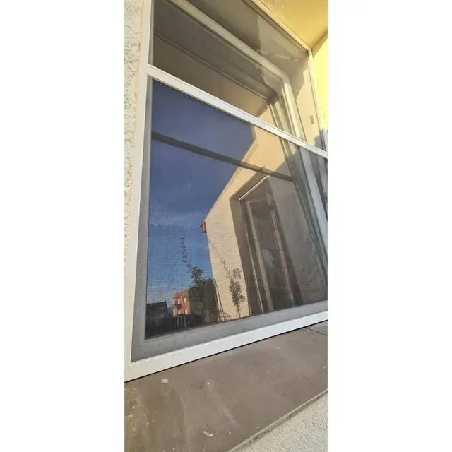 Ventana que refleja el cielo azul y la fachada del edificio cercano.