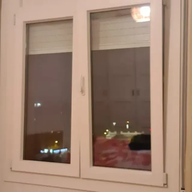 Ventana doble con marco blanco por la noche, con las luces de la ciudad visibles desde el exterior.