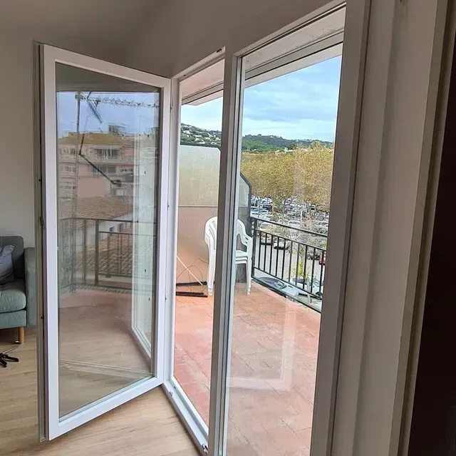 Puertas abiertas que dan a un balcón con suelo y barandilla rojos, con vistas a las colinas y al agua.