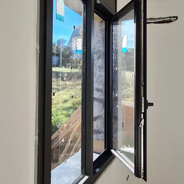 Ventana abierta con marco negro con vistas a un patio y a las casas vecinas en un día soleado.
