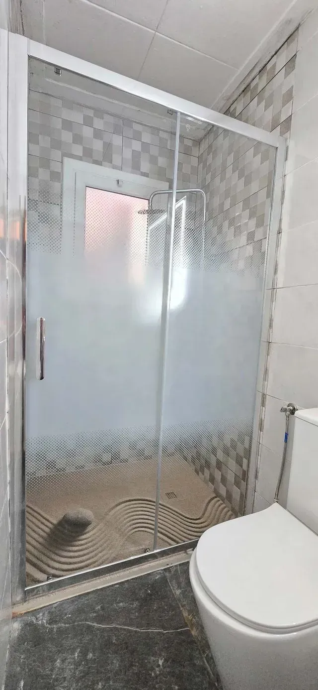 Baño pequeño con cabina de ducha de cristal, paredes alicatadas y un inodoro blanco.