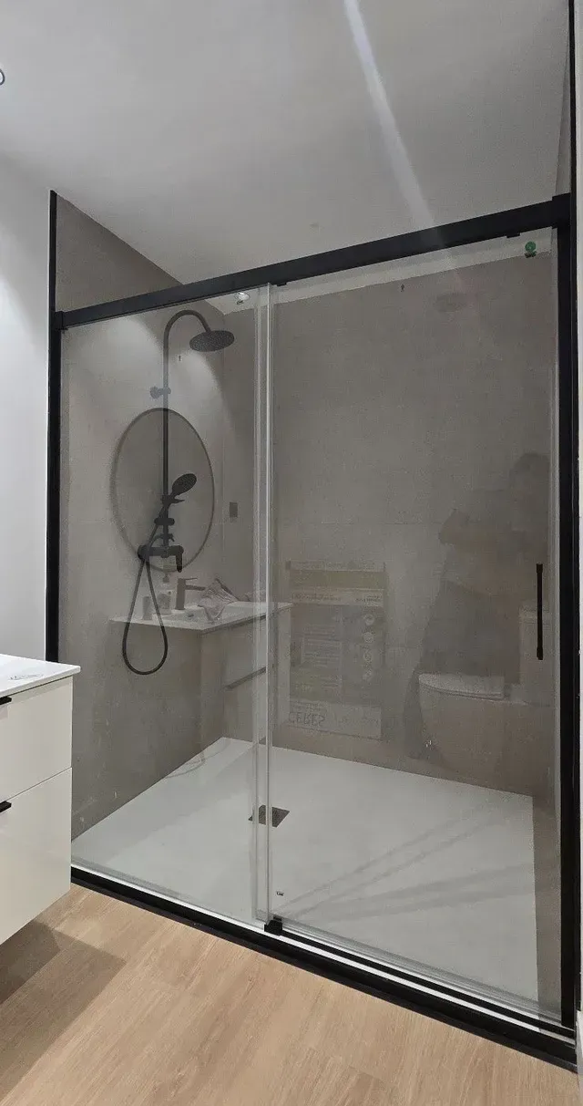 Mampara de ducha de cristal con paneles esmerilados y cabezal de ducha tipo lluvia en un baño moderno.