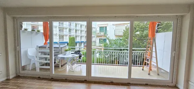 Amplio balcón con puertas corredizas de vidrio, muebles de exterior blancos y toldos naranjas con vistas a la vegetación.
