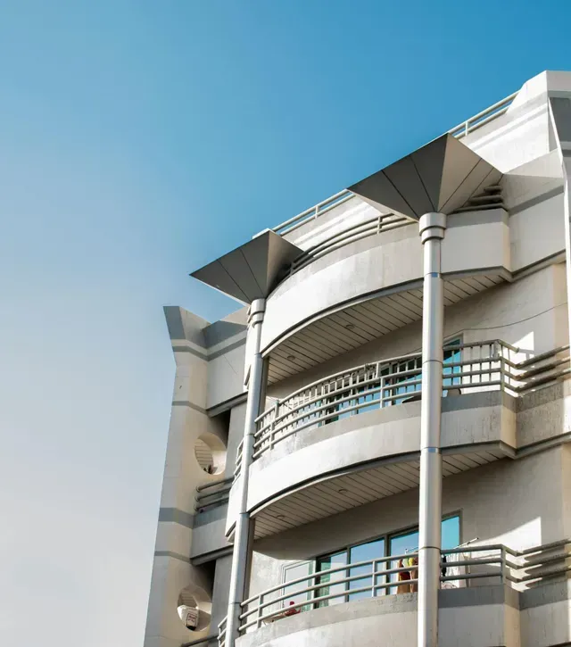 Edificio de apartamentos moderno de color blanco con balcones curvos y altas columnas contra un cielo azul.
