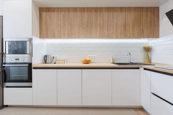 Cocina y sala de estar modernas de planta abierta con sofá color salvia, mesa de madera y grandes ventanales.