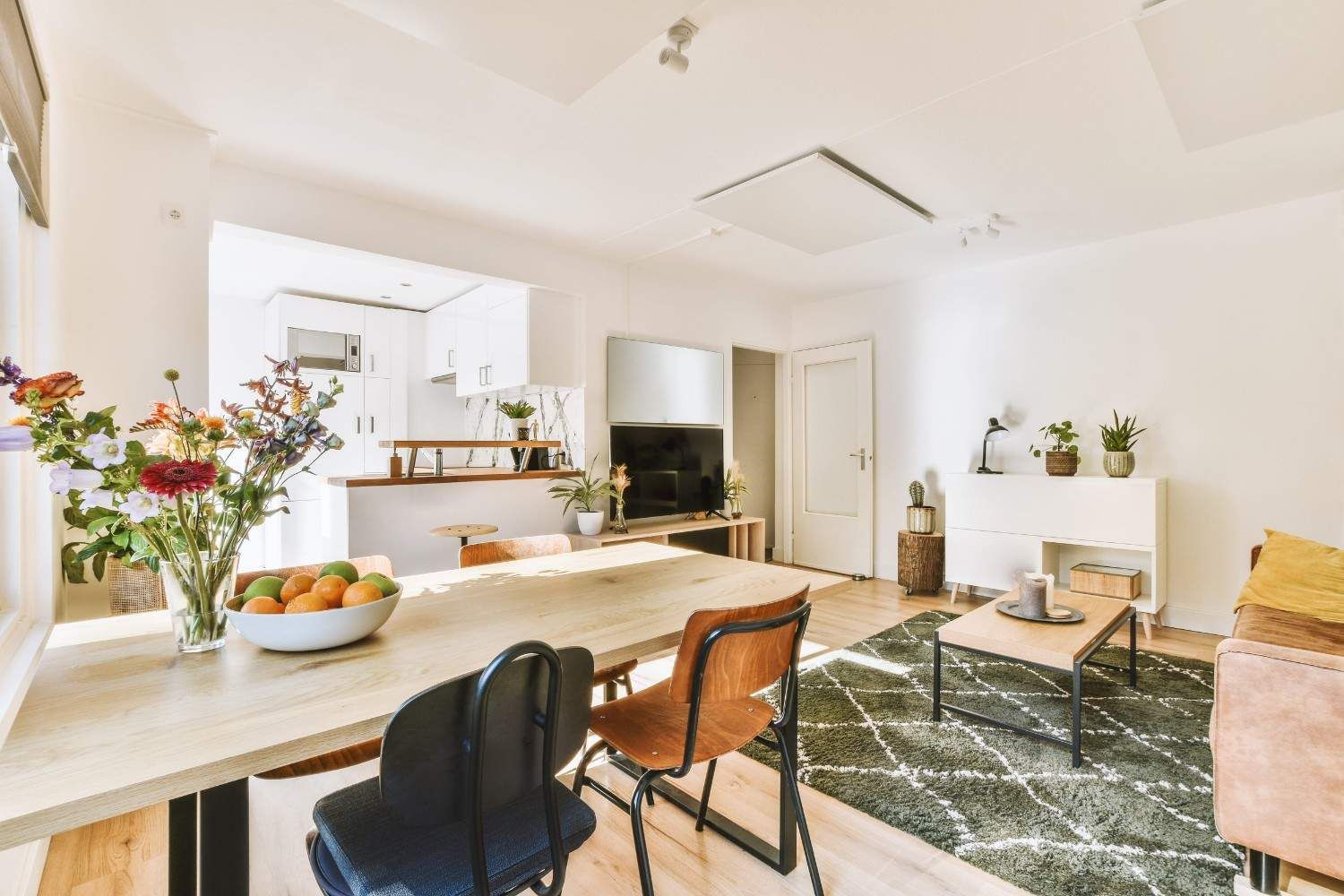 Luminoso salón moderno con mesa de comedor, sofá, mesa de centro y plantas en un espacio diáfano bañado por el sol.