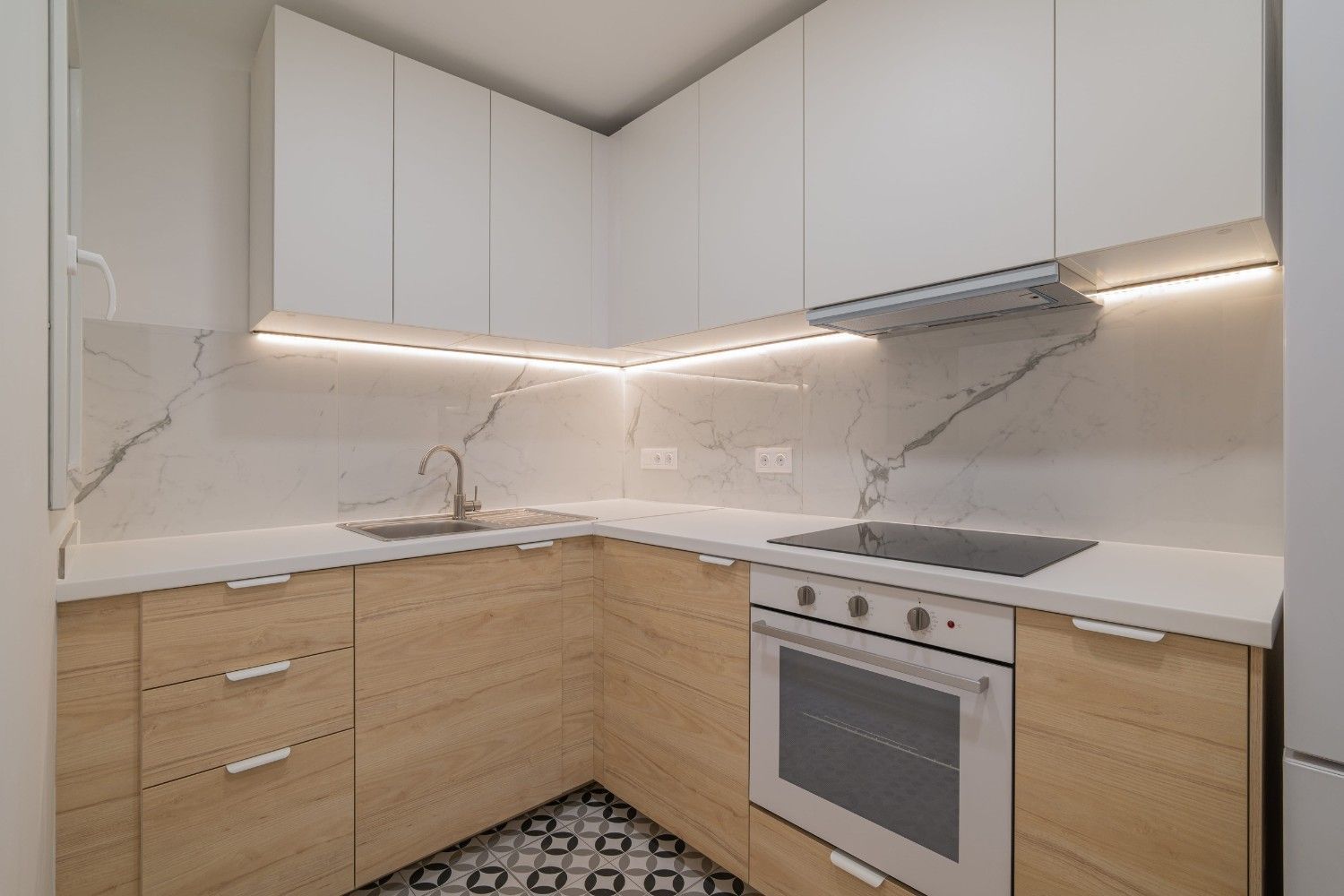 Cocina moderna con isla de mármol, armarios blancos, suelos oscuros y lámparas colgantes.