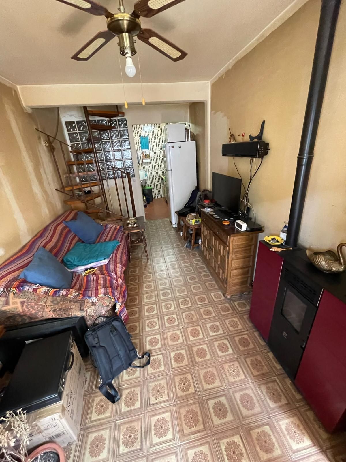 Habitación vacía de color beige con suelo de parqué, ventana, radiador y pared revestida de paneles de madera.