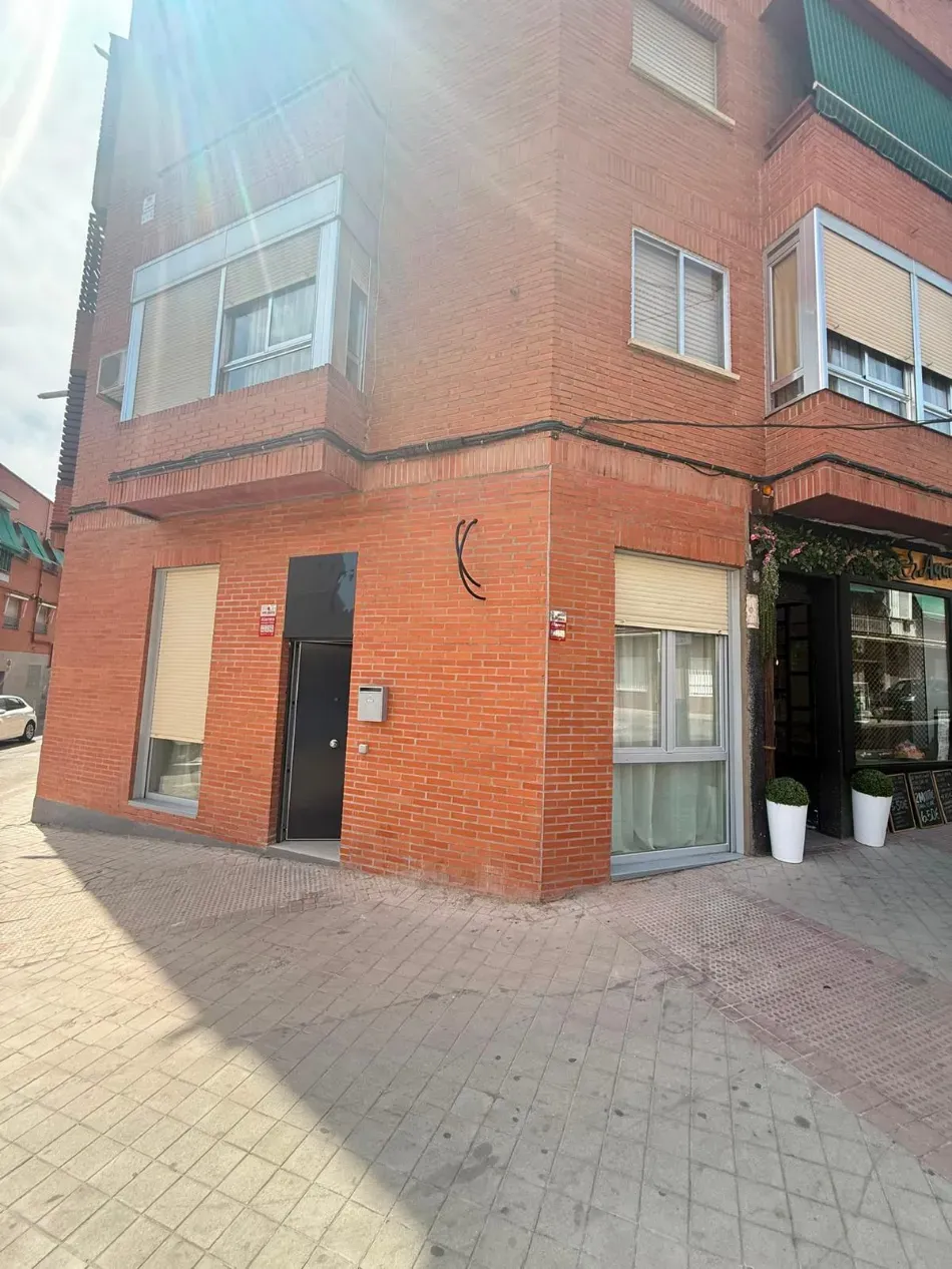 Edificio de esquina de ladrillo rojo con ventanas de marcos blancos y una pequeña entrada cubierta en una calle pavimentada.