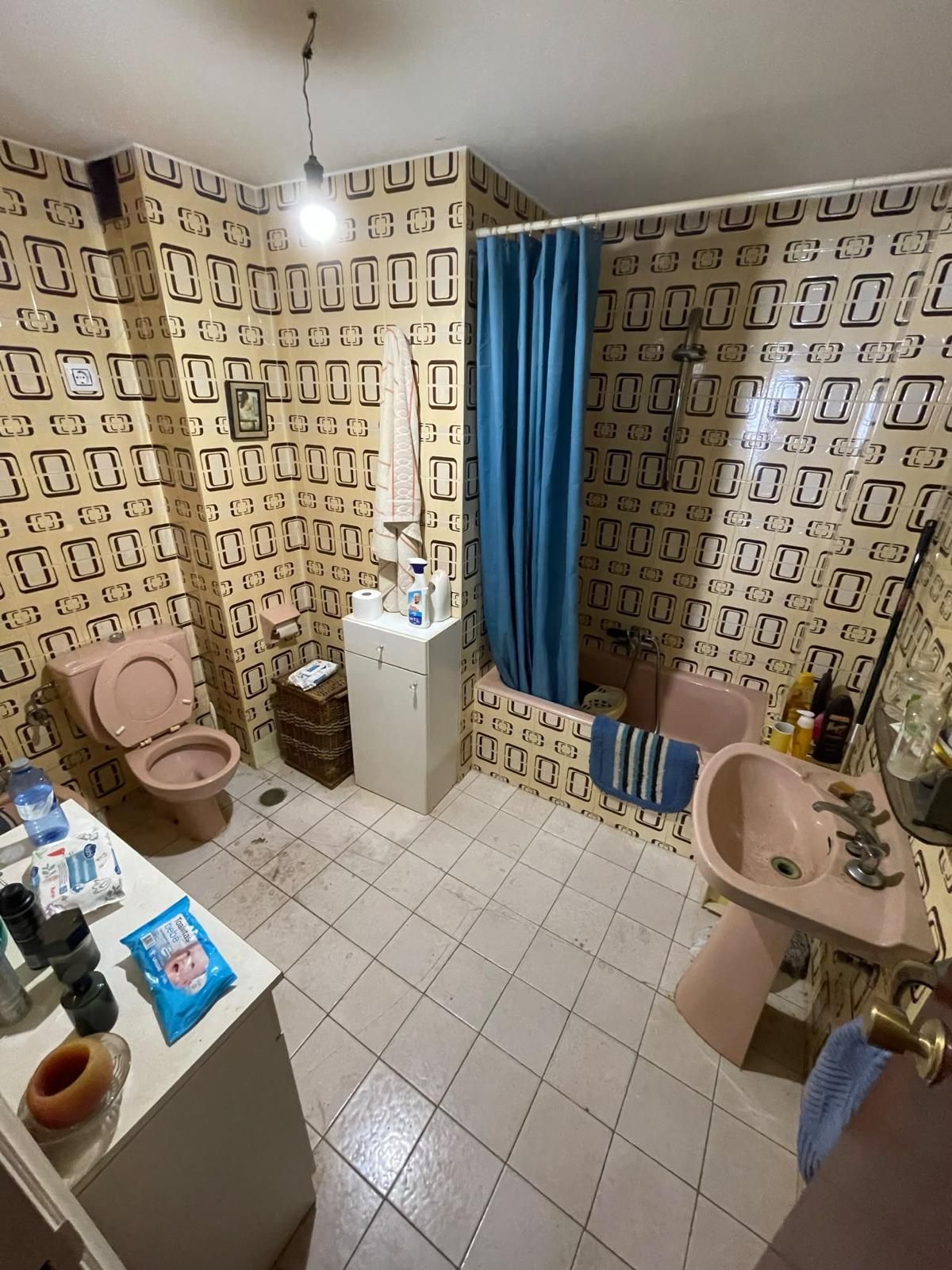Habitación vacía de color beige con suelo de parqué, ventana, radiador y pared revestida de paneles de madera.