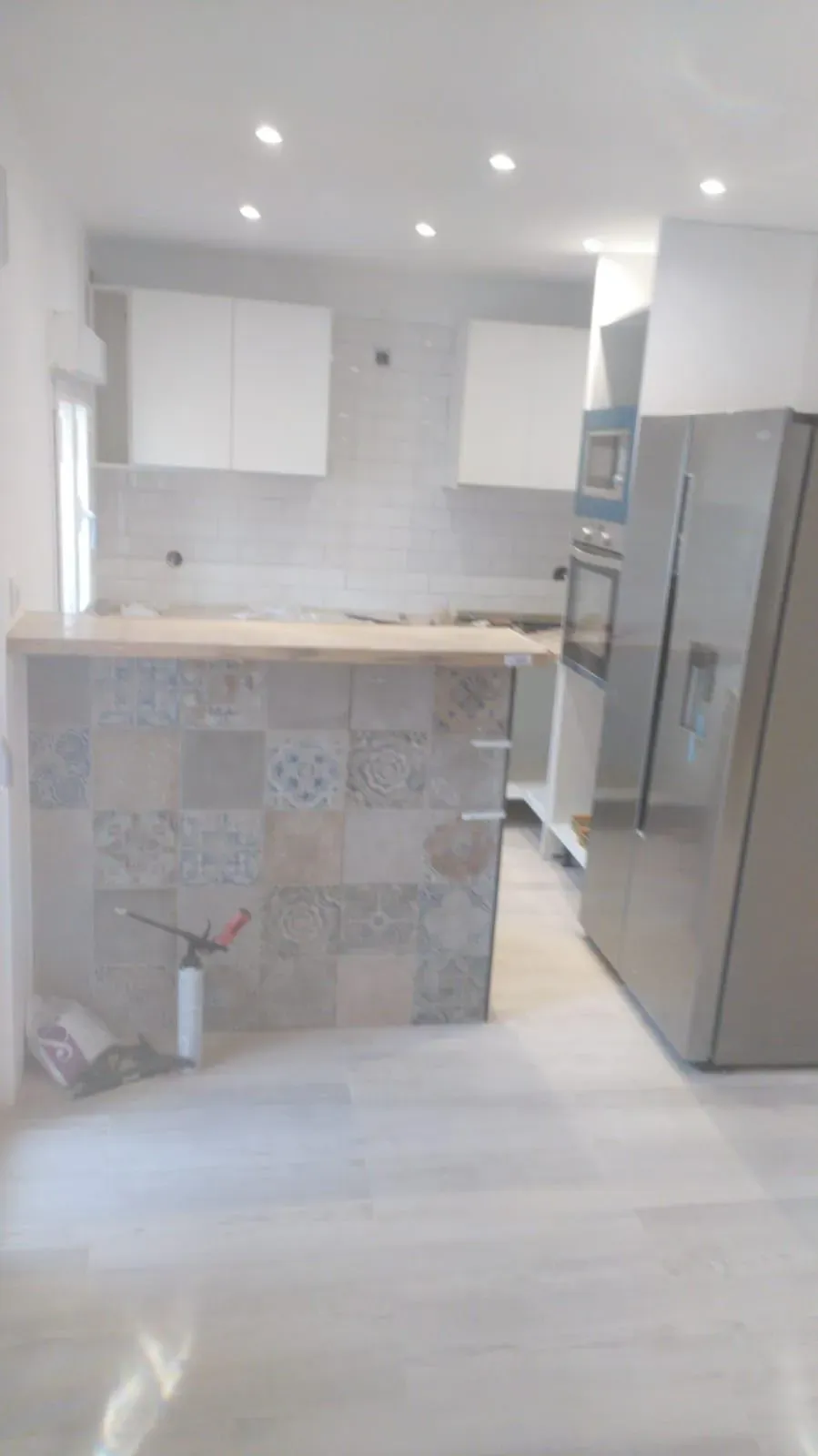 Cocina moderna con gabinetes blancos, salpicadero de azulejos grises, isla y refrigerador de acero inoxidable.