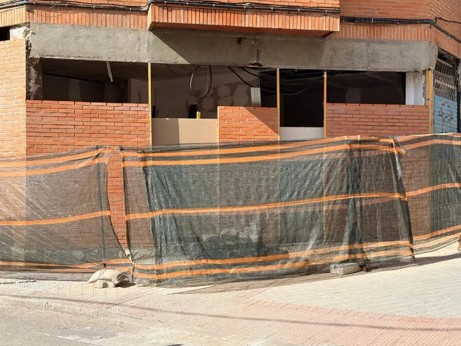 Estructura de ladrillo parcialmente construida detrás de una valla de construcción verde y una red naranja.