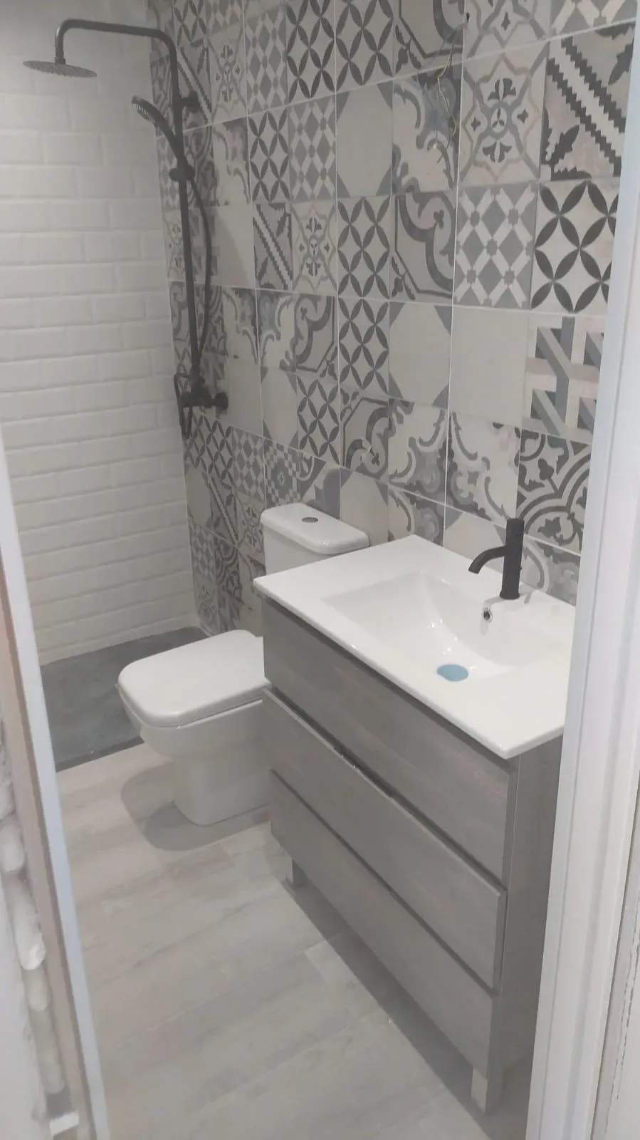 Baño moderno con inodoro, lavabo con tocador y zona de ducha con azulejos estampados.
