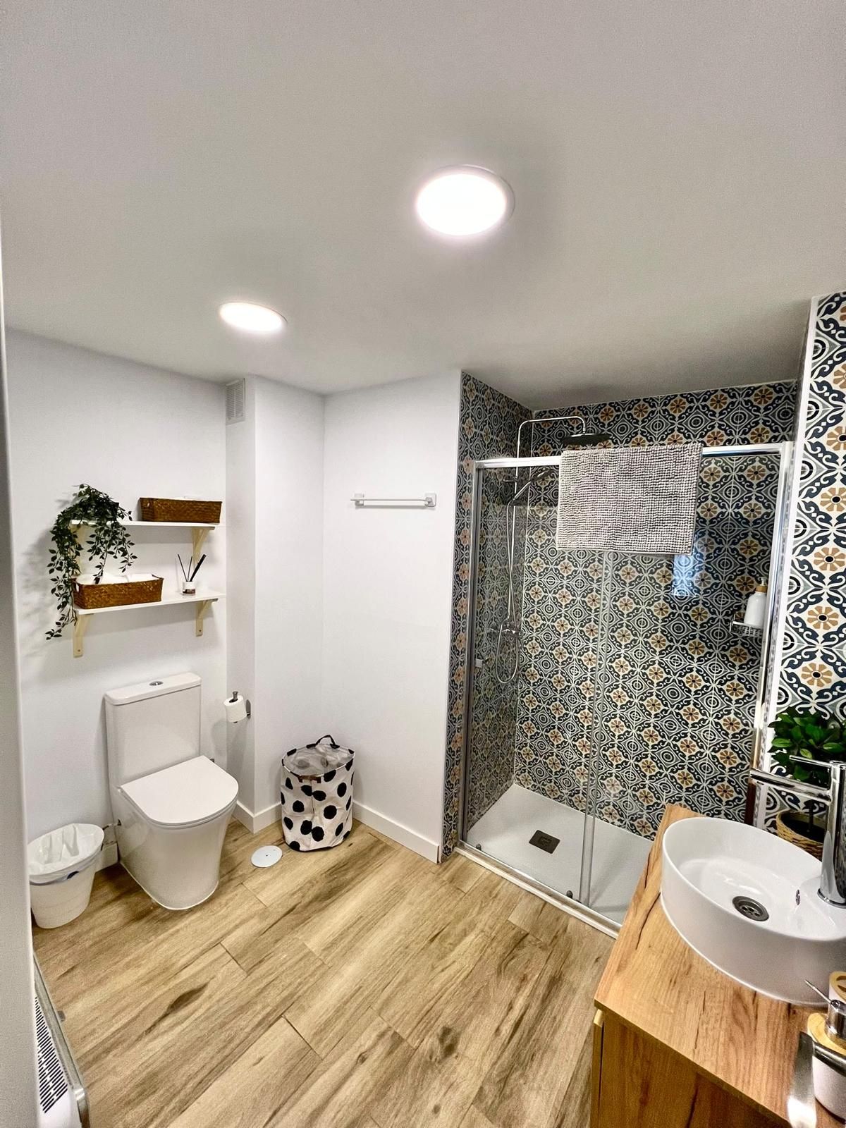 Acogedora sala de estar con sofá modular beige, televisor, alfombra turquesa, mesa de centro, estantes y planta colgante.