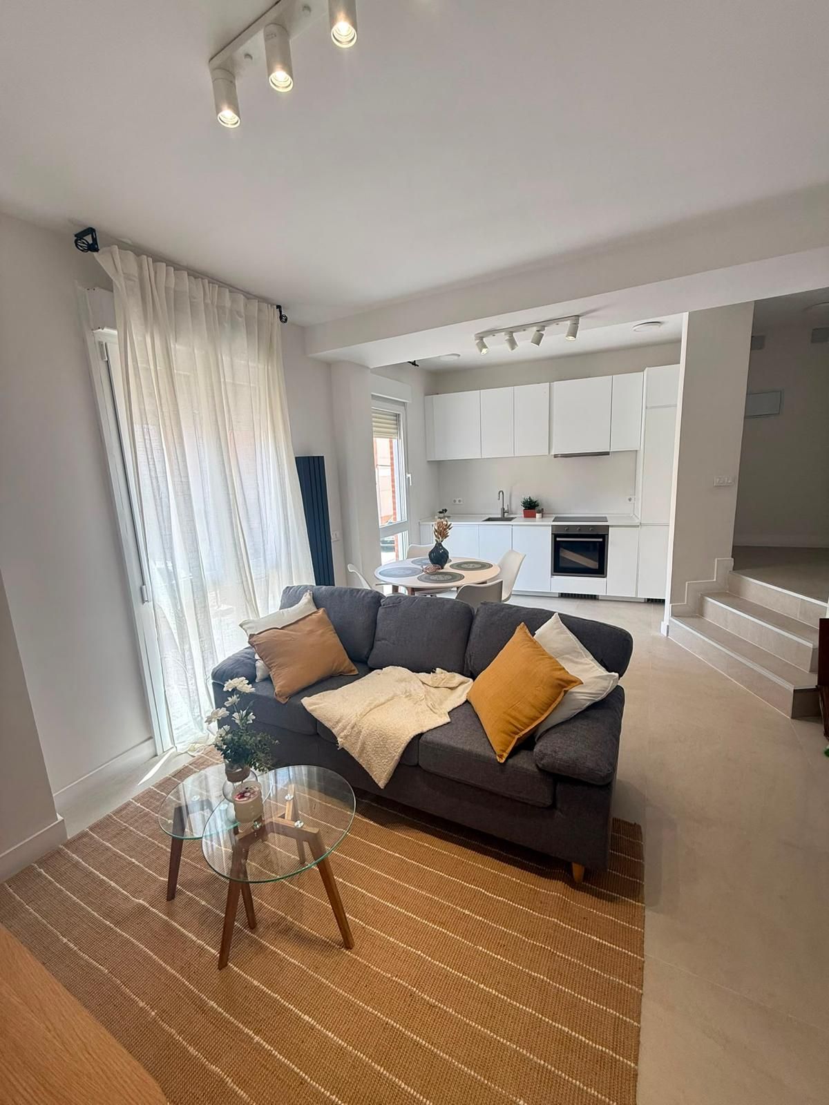 Acogedora sala de estar con sofá modular beige, televisor, alfombra turquesa, mesa de centro, estantes y planta colgante.