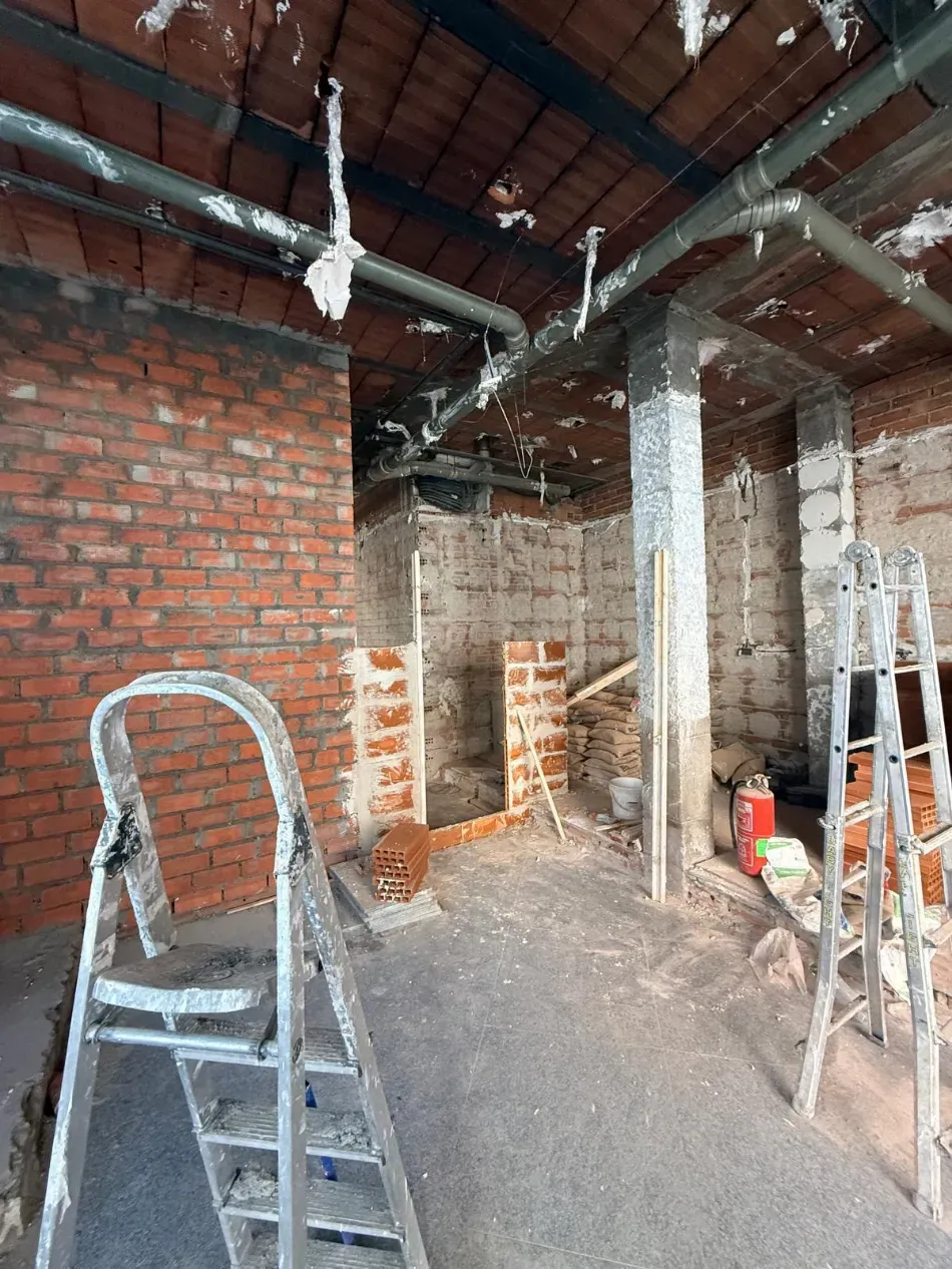 Habitación de ladrillo parcialmente construida con vigas expuestas, escaleras y escombros de construcción en el suelo.