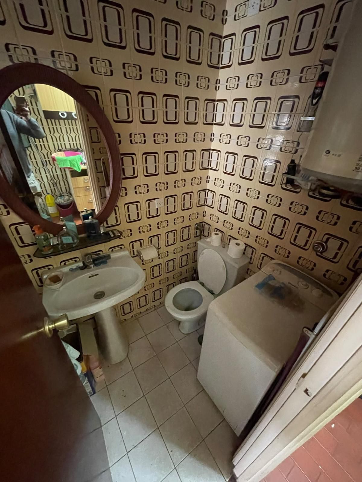 Habitación vacía de color beige con suelo de parqué, ventana, radiador y pared revestida de paneles de madera.