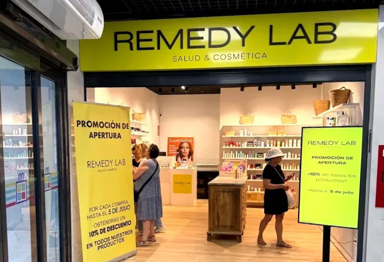Entrada a la tienda Remedy Lab con toldo amarillo y carteles promocionales. La gente mira dentro.