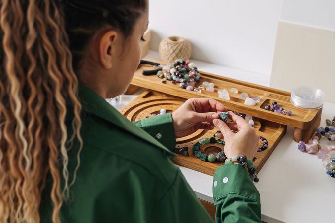 Une personne dispose des perles dans un plateau en bois posé sur une table, avec du matériel de loisirs créatifs éparpillé à proximité.