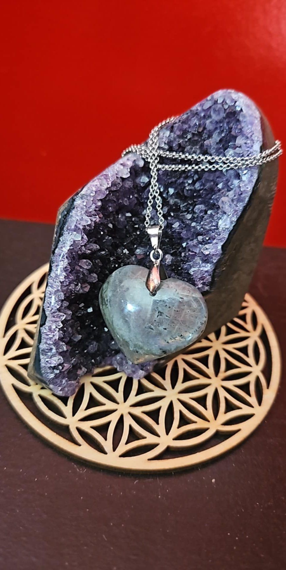 Collier pendentif en forme de cœur sur un présentoir en cristal avec une base géométrique en bois.