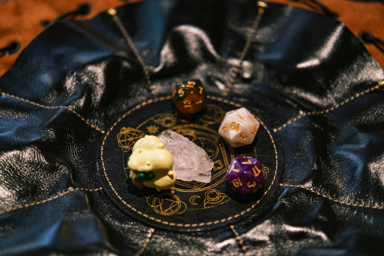 Quatre petits charmes en forme de dés sur une pochette noire à cordon avec un imprimé circulaire doré