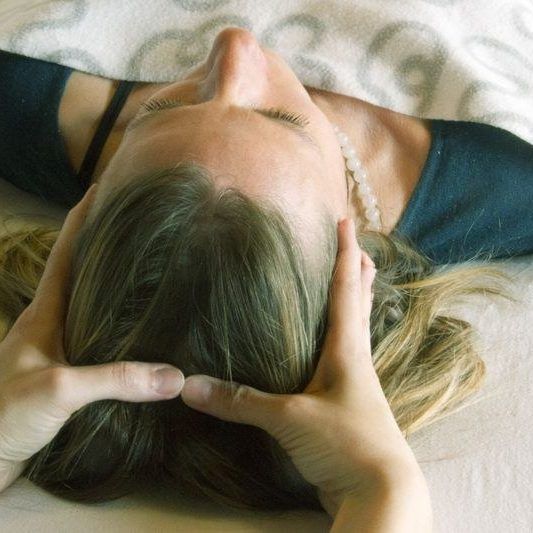 Une personne masse le crâne d'une femme allongée.
