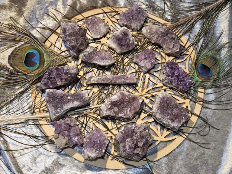 Mandala de plumes de paon avec des cristaux violets disposés en cercle sur fond gris