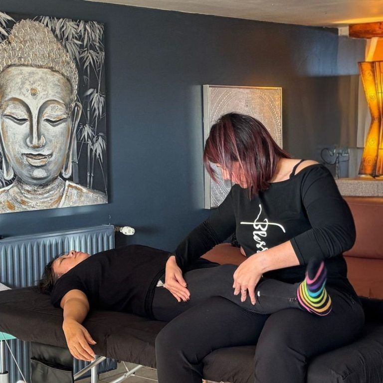 Une femme masse une personne allongée dans une pièce aux murs sombres et ornée d'un tableau de Bouddha.