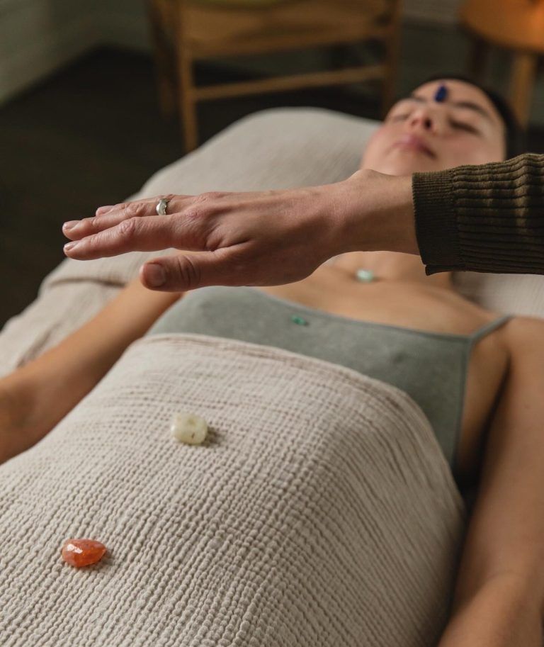 Une personne allongée sur une table de soin bien-être, des pierres posées sur le torse et une main au-dessus d'elle.