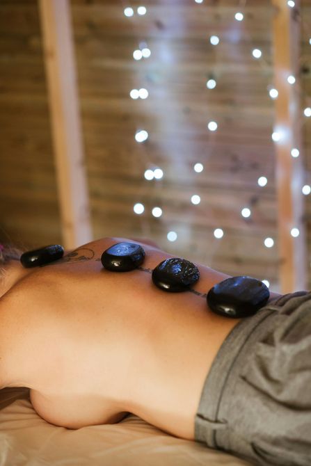 Des pierres chaudes sont posées sur le dos d'une personne lors d'un massage, avec une lumière douce en arrière-plan.