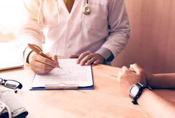 Un médico está escribiendo en un portapapeles mientras habla con un paciente.