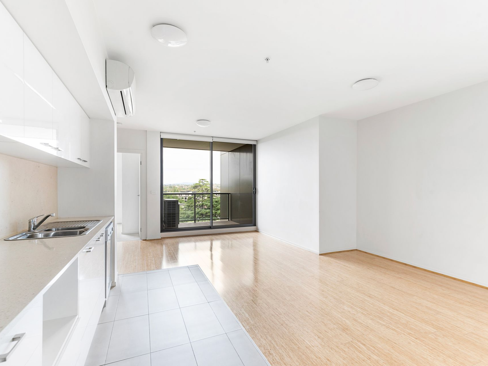 Intérieur d'appartement vide et lumineux avec cuisine, grande fenêtre et parquet.