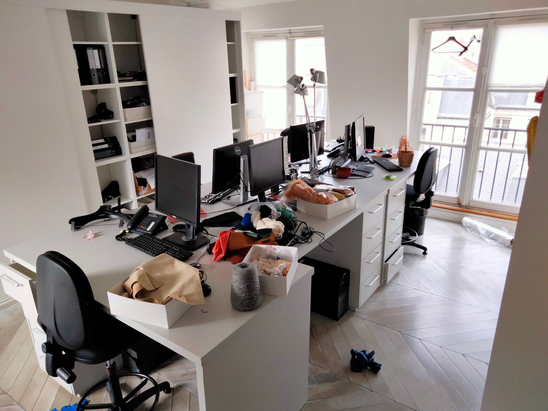 Espace de travail de bureau avec bureaux encombrés, ordinateurs et une étagère blanche intégrée.