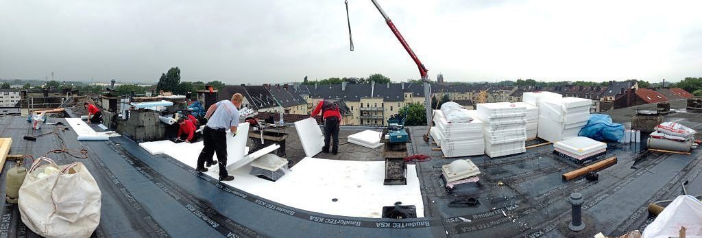 Arbeiter montieren weiße Dämmplatten auf einem großen, flachen, mit dunklen Materialien bedeckten Dach.