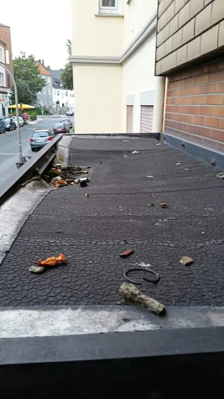 Eine flache Dachfläche, bedeckt mit verwittertem, schwarzem Dachmaterial und verstreuten Trümmern.