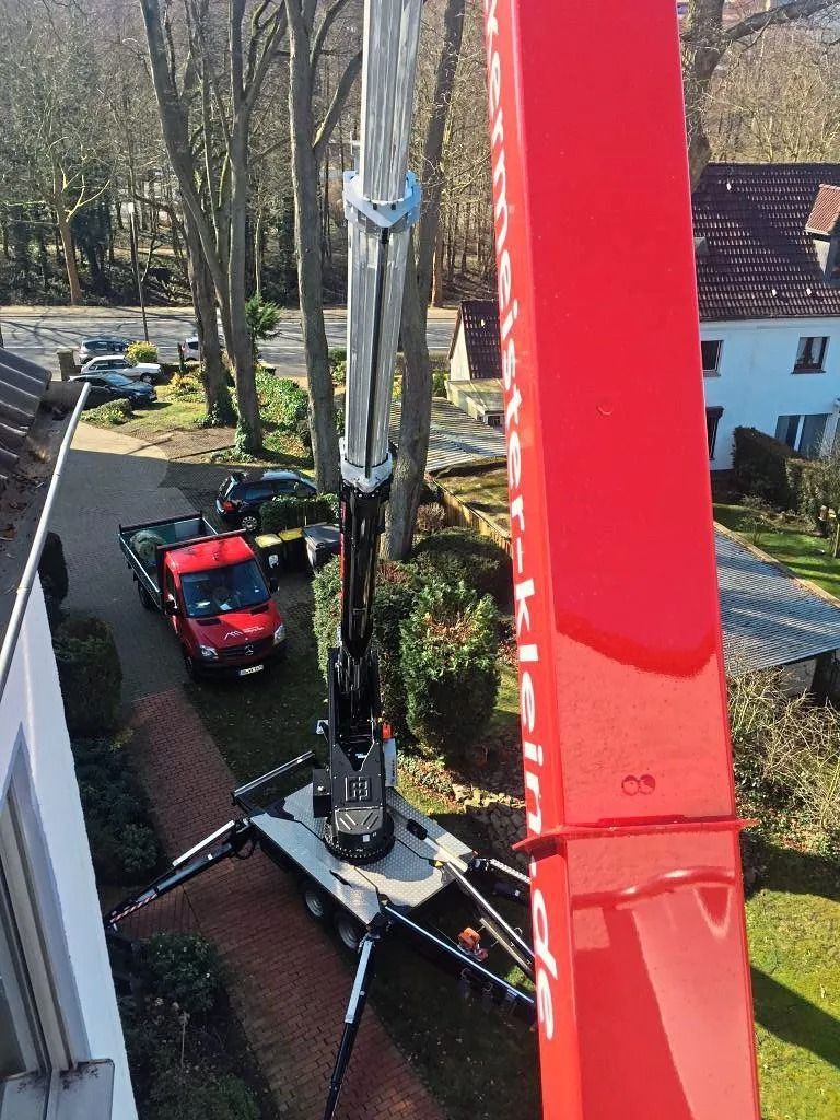 Aufnahme aus der Vogelperspektive: Ein roter Kranausleger ragt von einem Fahrzeug nach oben.