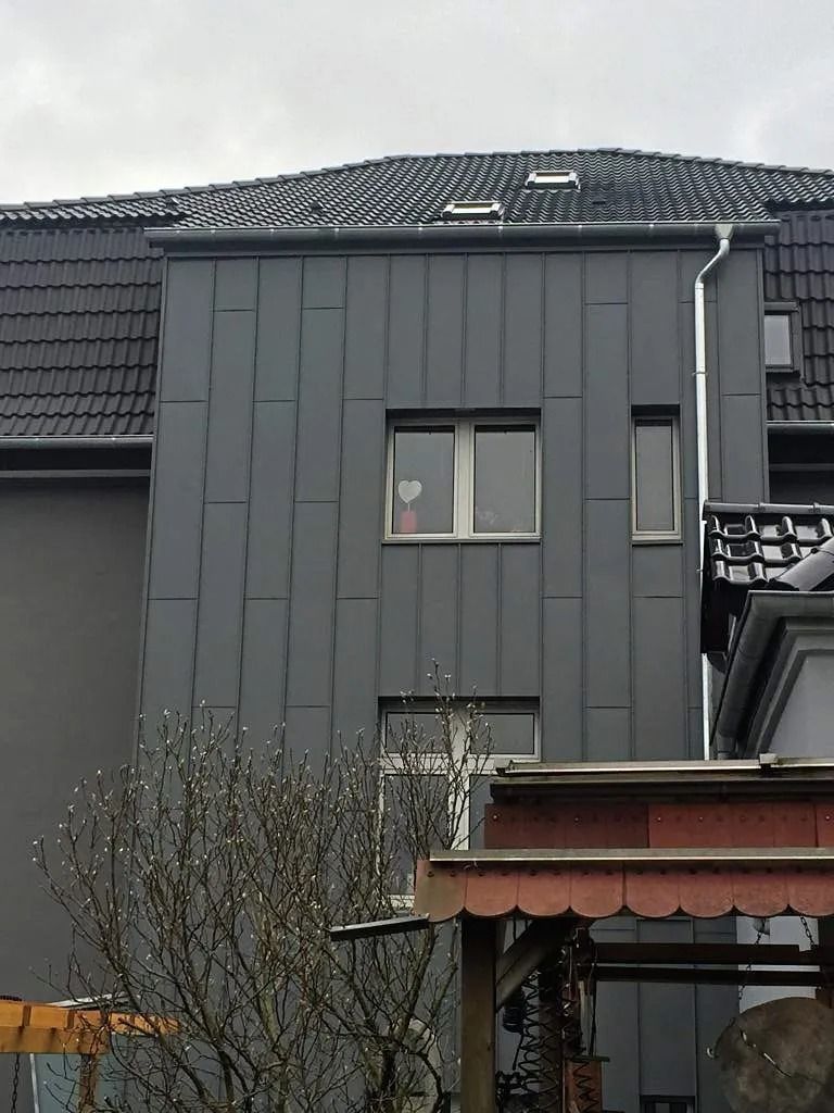 Eine dunkelgraue, mit Metallpaneelen verkleidete Gebäudefassade mit zwei rechteckigen Fenstern.