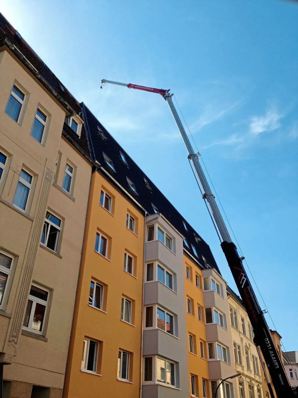 Ein Ausleger eines Krans in Richtung des dunklen Daches einer Reihe farbenfroher Wohnhäuser.