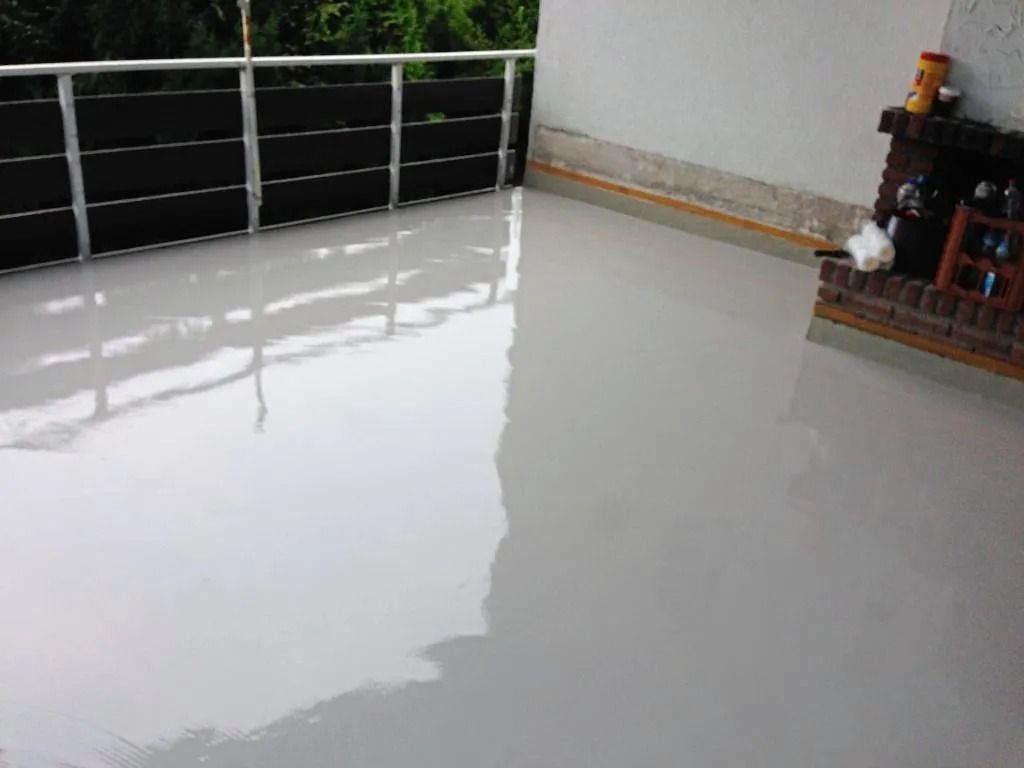 Ein glänzender, hellgrauer Epoxidharzboden auf einem Außenbalkon mit schwarzem Metallgeländer und einem gemauerten Kamin.