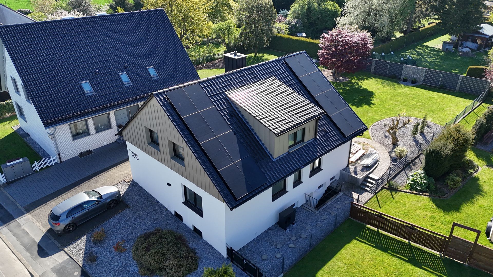 Ein weißes zweistöckiges Haus mit dunklem Ziegeldach und Balkon, gelegen an einem grünen Grashang unter bedecktem Himmel.