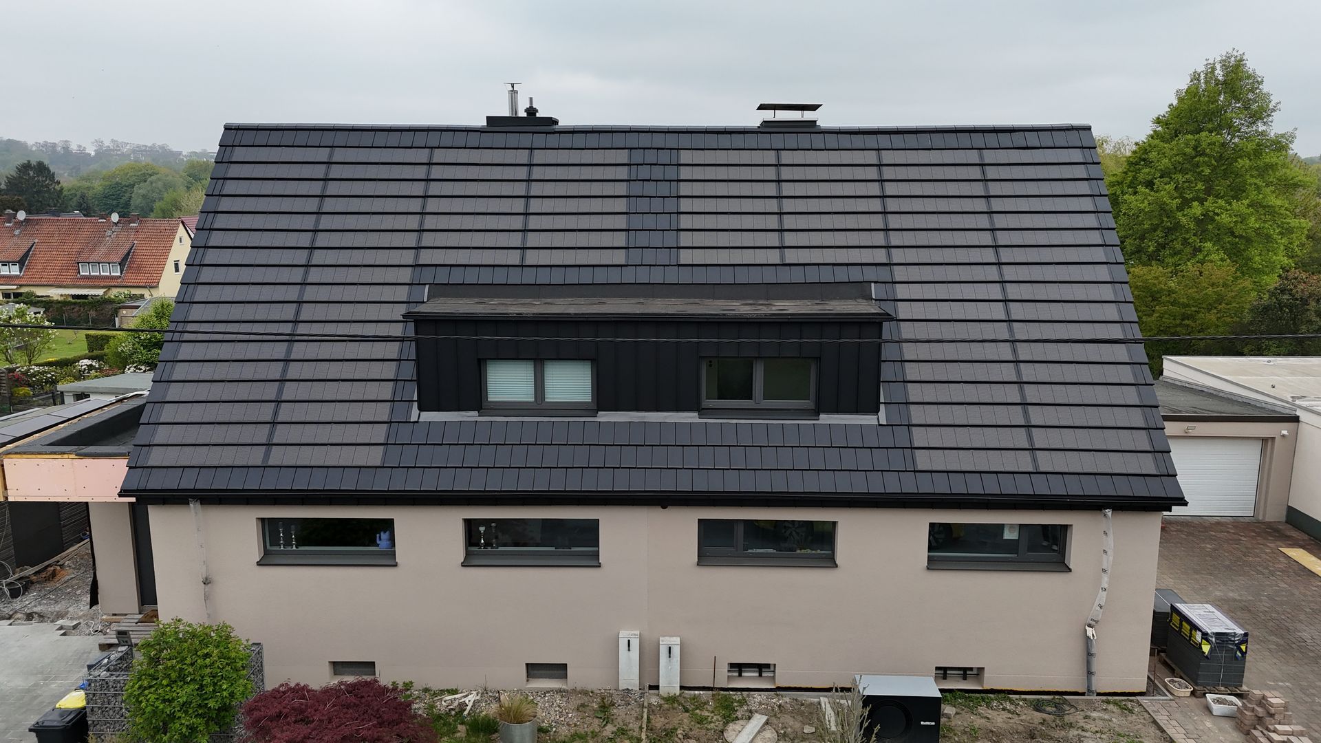 Ein modernes Haus mit dunklem Ziegeldach, zwei Dachfenstern, einem Dachgaubenfenster und heller Backsteinfassade.