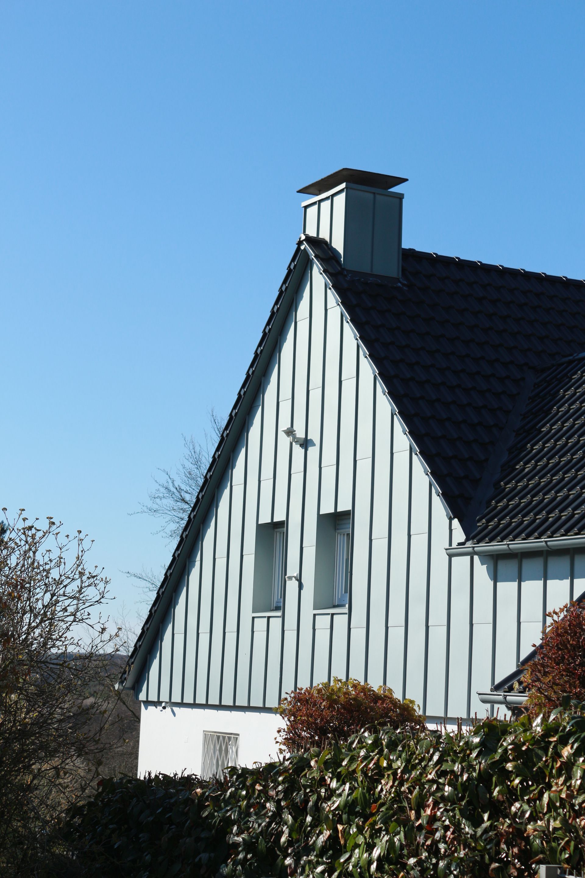 Weißes Haus mit steilem, schwarzem Dach und Dachgauben vor blauem Himmel