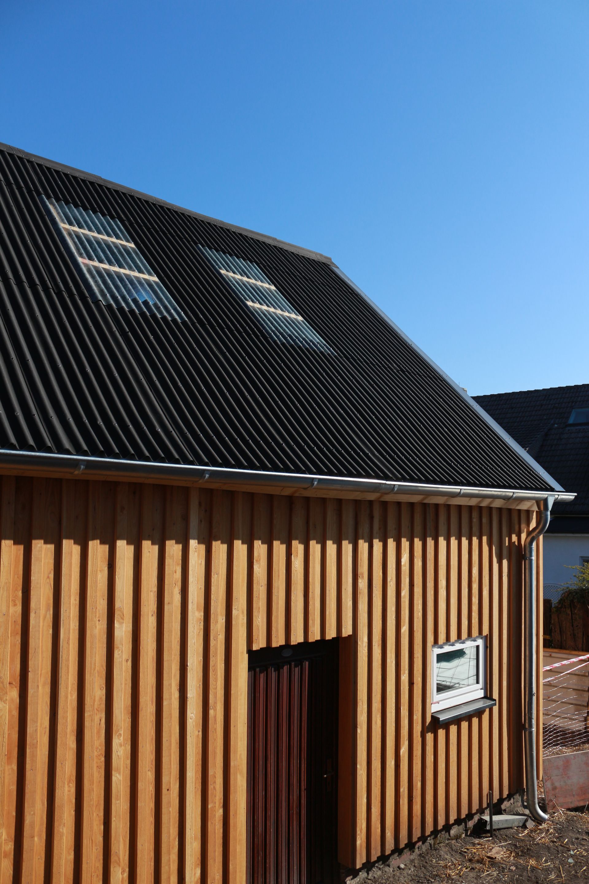 Holzhaus mit schwarzem Dach und Dachgauben unter klarem, blauem Himmel