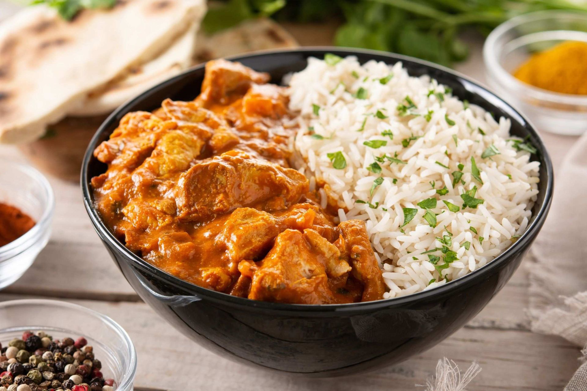 Un tazón de pollo tikka masala y arroz sobre una mesa de madera.