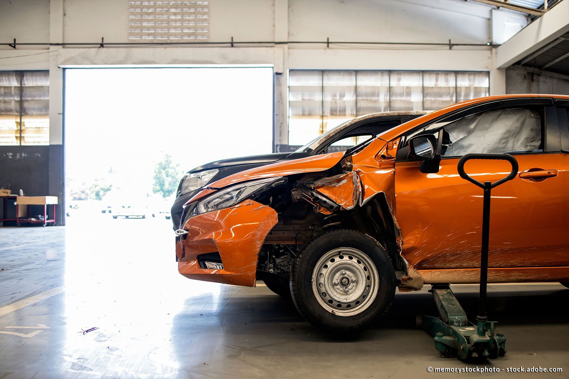 ein orangefarbenes Unfallfahrzeug steht in einer großen Werkstatt