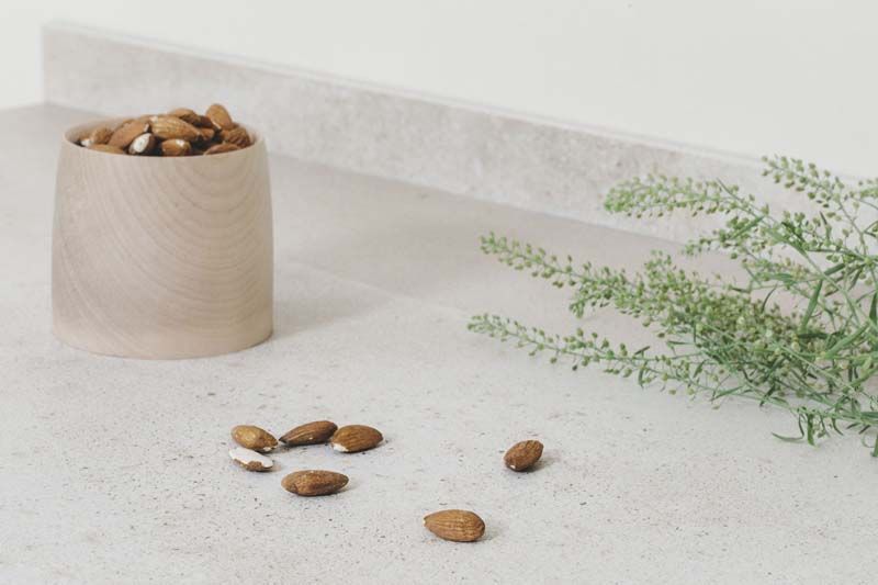 Un cuenco de almendras reposa sobre un mostrador al lado de una planta.