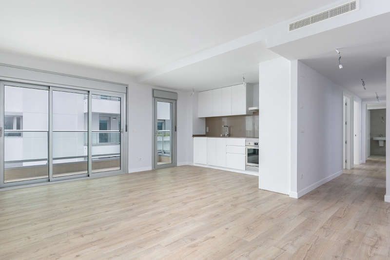 Una sala de estar vacía con pisos de madera y puertas corredizas de vidrio que conducen a una cocina.